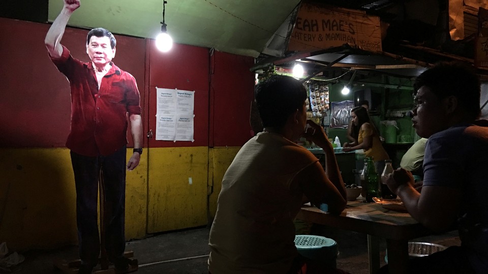 A life-size cut-out of President-elect Rodrigo Duterte looms over diners at a street stall in the center.