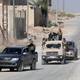 Turkey-backed Syrian rebel fighters ride on vehicles on a dusty road.