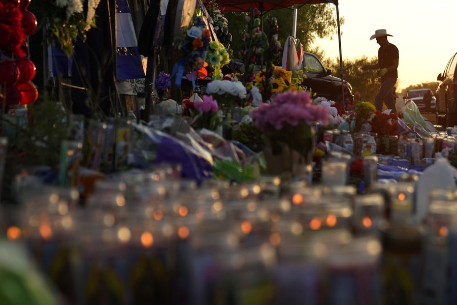 A person adds crosses to a makeshift memorial filled with candles and floral bouquets.