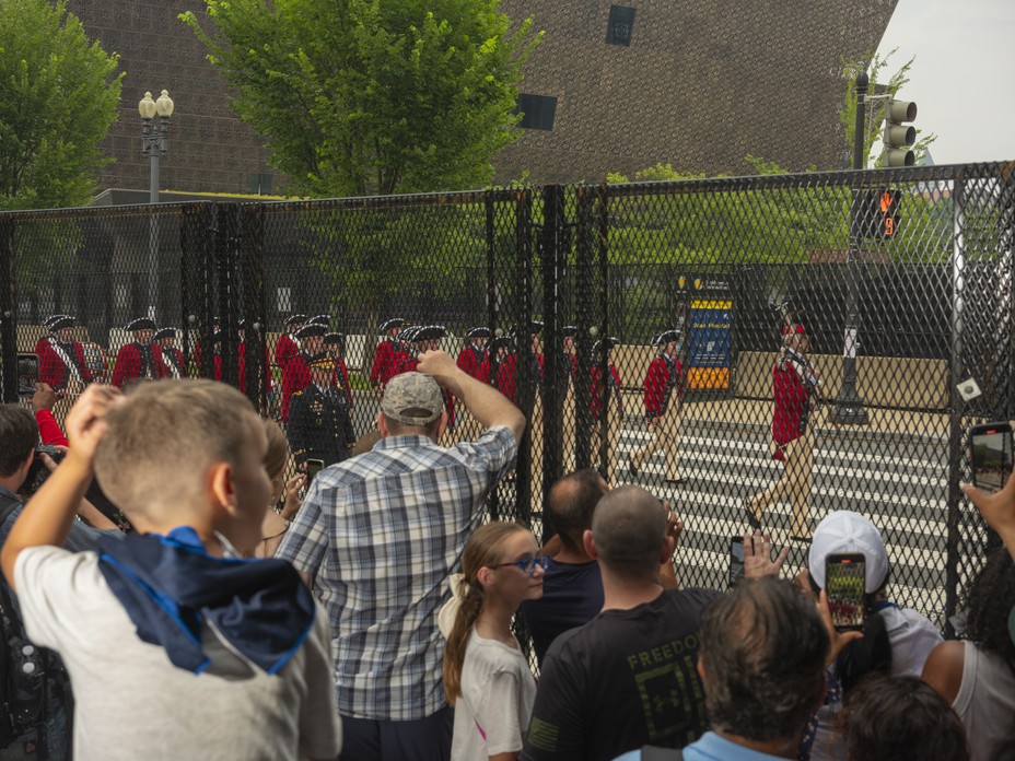 Picture of crowds watching the Old Guard Fife and Drum Corps from behind barricades near the National Museum of African American History.