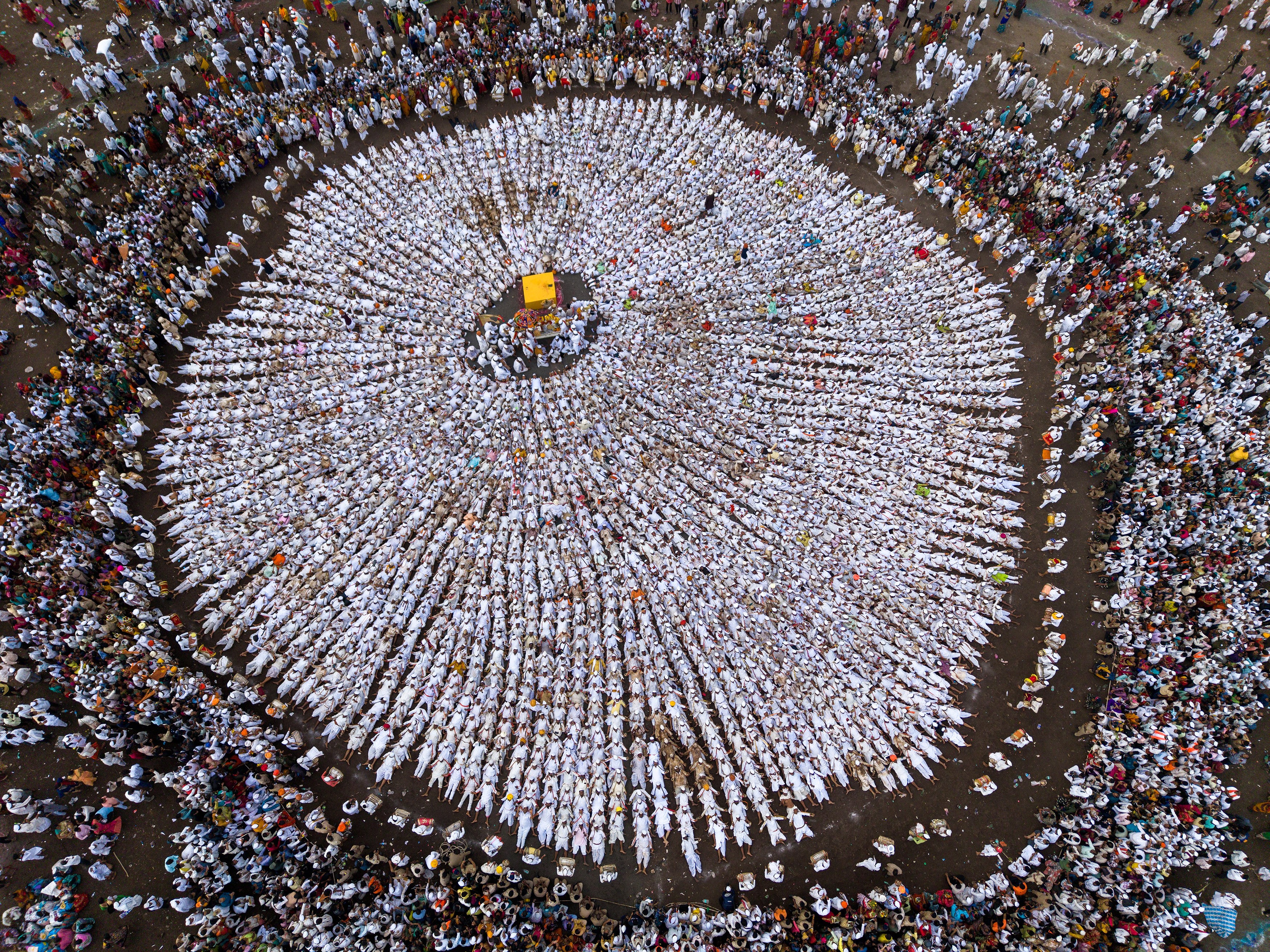 A top-down view of hundreds of worshippers dressed in white, arranged in rows, forming a circle around a central shrine