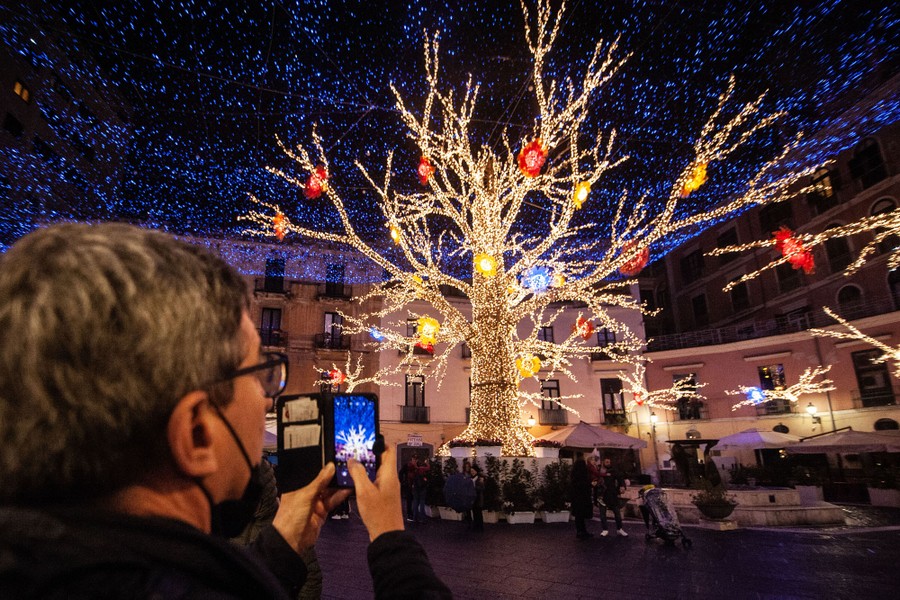 A person takes a picture of a tree covered in lights.