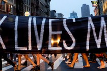 People walking across a crosswalk behind a Black Lives Matter banner