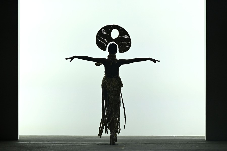 A model wearing a large headpiece walks with their arms out in silhouette.
