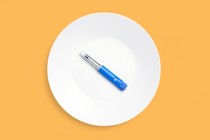 A blue Ozempic sits on a white plate on an orange background