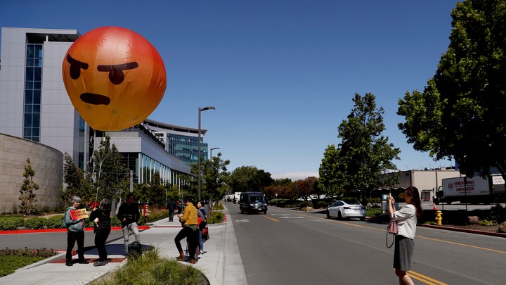 People hold a balloon version of the "angry" emoji.