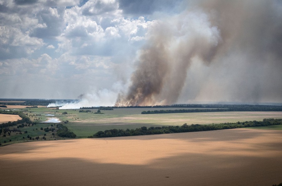 Smoke rises above farm fields, seen from a distance.