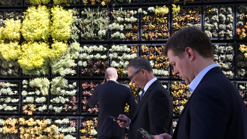 People look at their cellphones in front of a wall garden during the Milken Institute Global Conference in Beverly Hills, California, in May 2017.