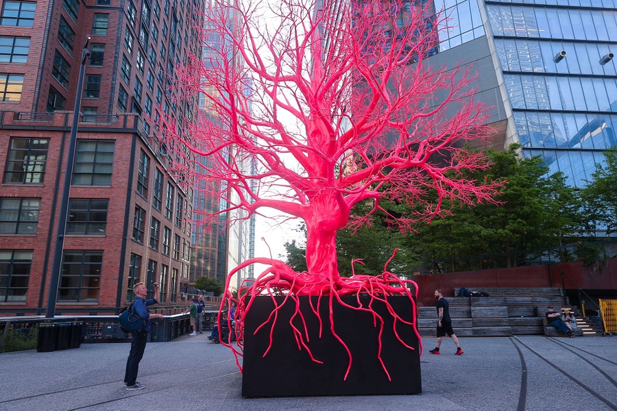 A bright-red-pink tree sculpture stands in a city.