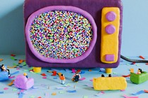 Miniature people standing and sitting on couches surround a TV with a pixelated screen