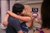 A person uses a cellphone to take a picture of a couple kissing.