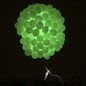 A performer hangs beneath a huge cluster of glowing green balloons.