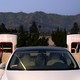 A photograph of a white Tesla between two superchargers.