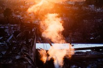 A color photograph of smoke rising in orange light above burned homes.