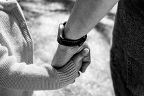 Black-and-white close-up image of an adult hand holding a child's hand