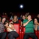 A group of people in a movie theater make scared faces and clutch each other.