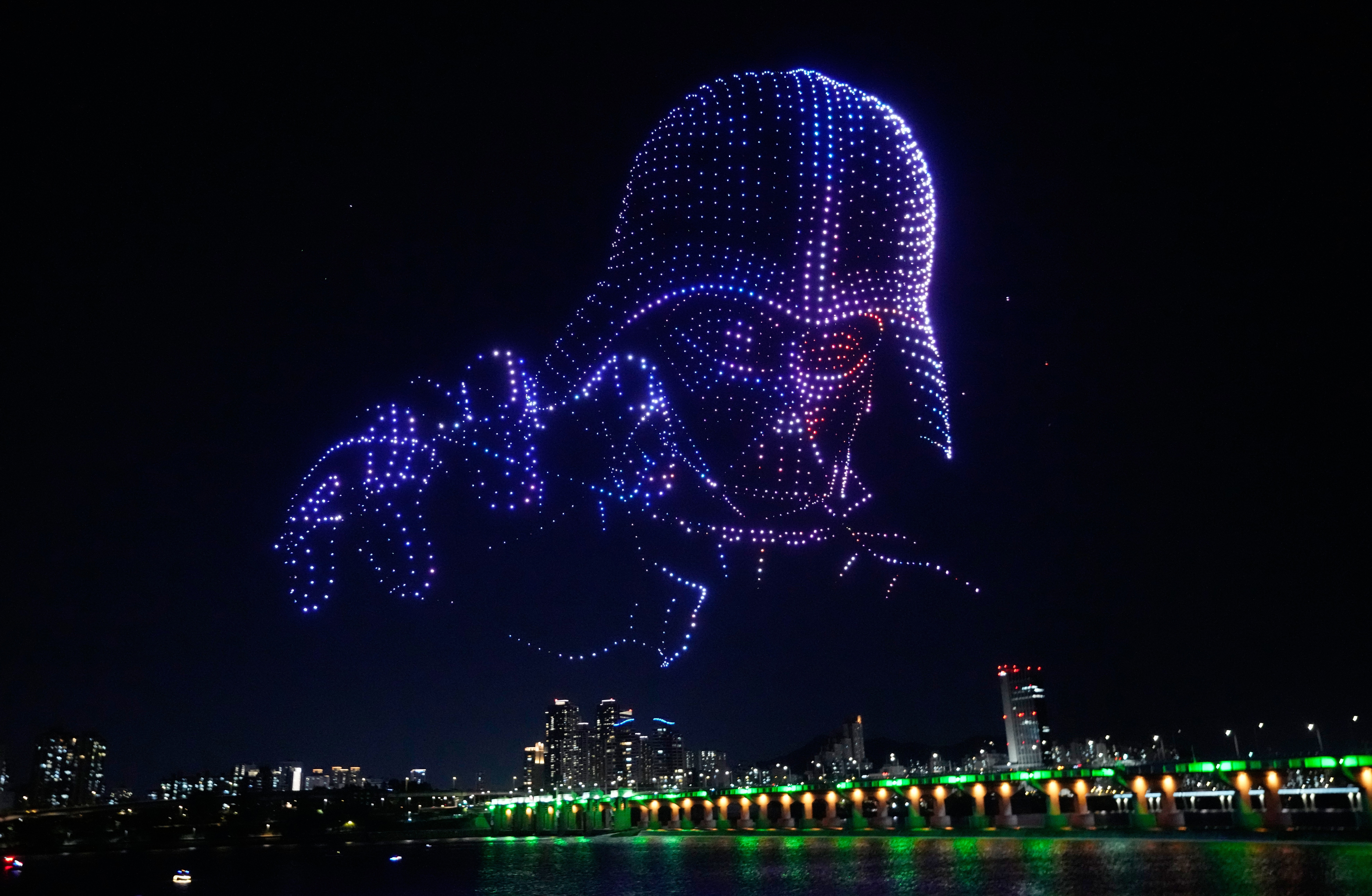 Illuminated drones form the shape of Darth Vader in the sky above a city during a drone show.