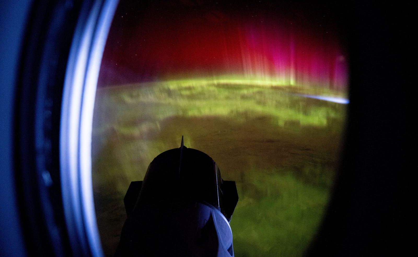 Peering through the window of a spacecraft, looking at a spectacular auroral light show.