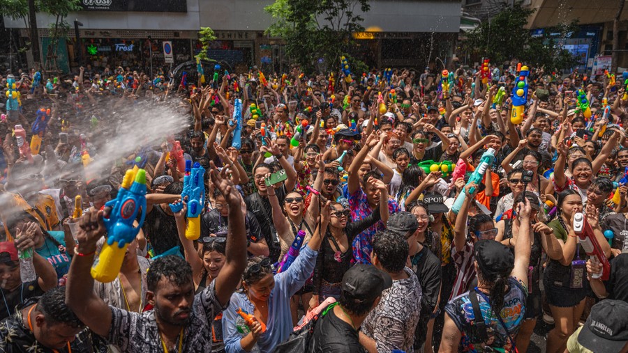 A large crowd of people dance in a street, many holding up colorful water guns.