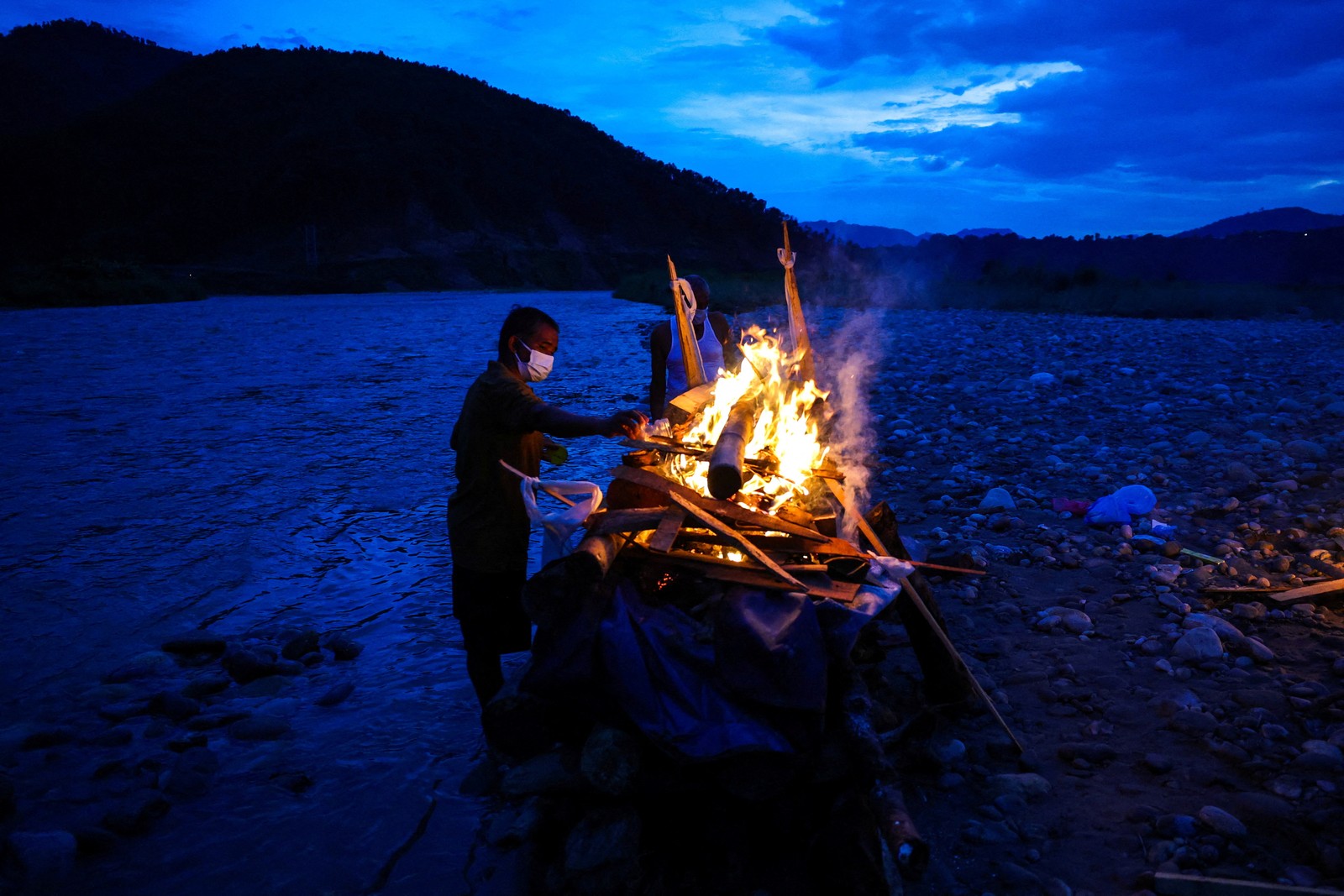 A person lights a funeral pyre beside a river.