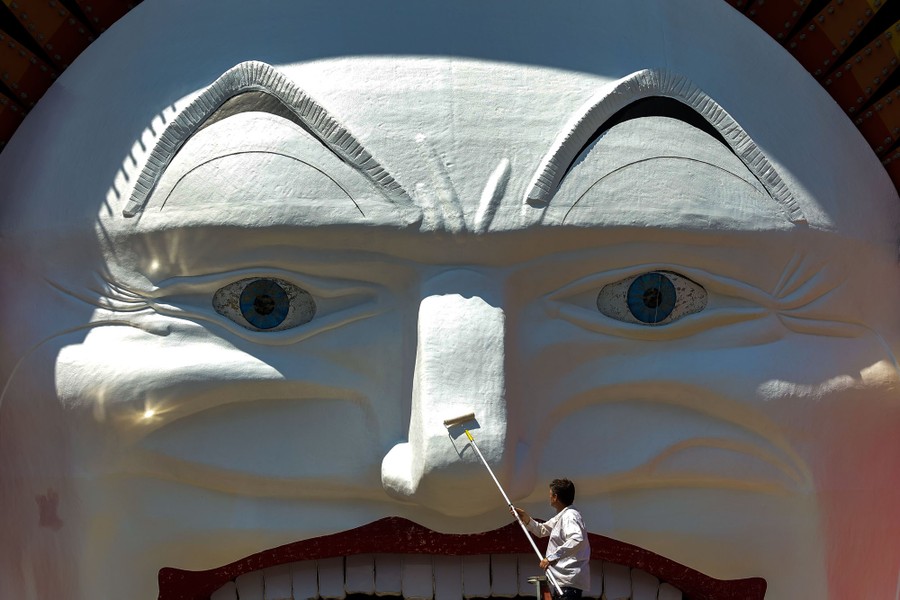 A person uses a roller to paint the nose of a very large sculpture of a face.