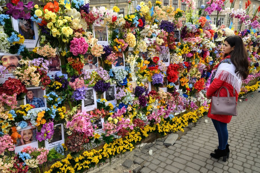 A woman looks at a temporary memorial wall, covered by portraits and floral arrangements.