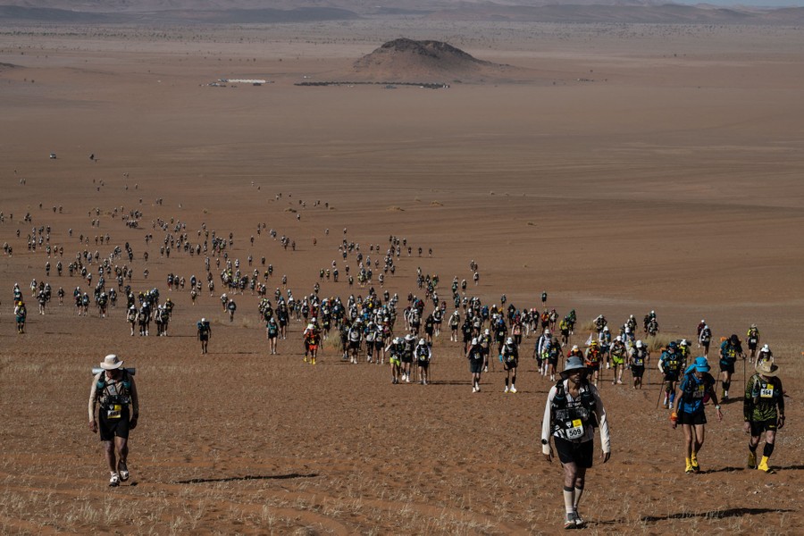 A view across a broad and flat desert valley with dozens of competitors walking toward the camera