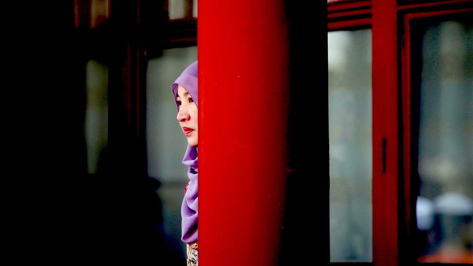 A woman stands behind a pillar during the Eid al-Adha festival at a Chinese mosque.