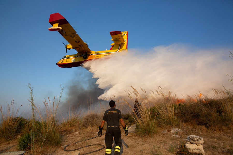 A firefighter looks on as an aircraft drops water to extinguish a wildfire.