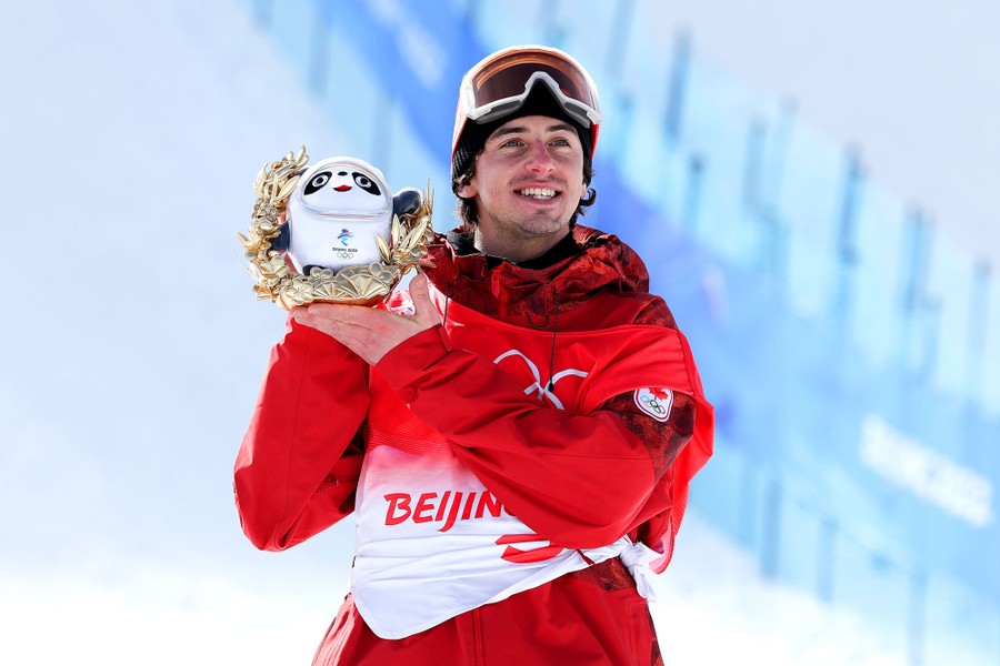 A medal-winning athlete holds up a small panda statue during a ceremony held at the base of a ski slope.