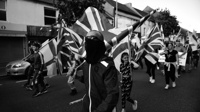 Loyalists holding the Union Jack walk down a street.