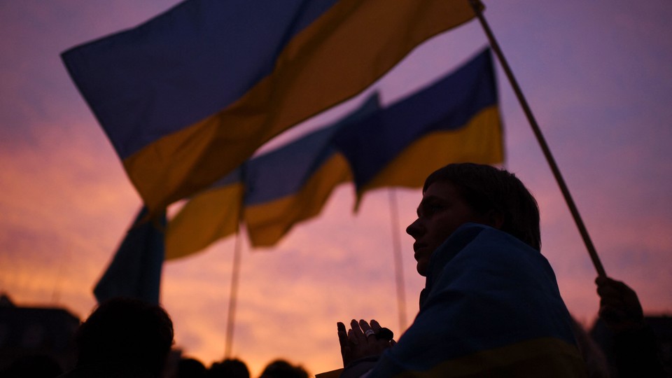 A crowd waving Ukrainian flags in front of sunset sky.