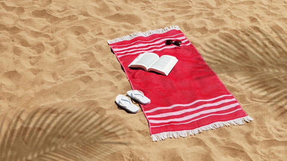 A red towel with a book, flip flops, and sunglasses on the beach