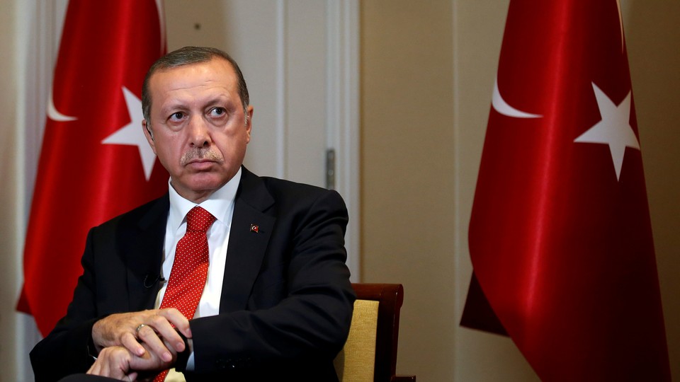 President Erdogan sits between two Turkish flags.