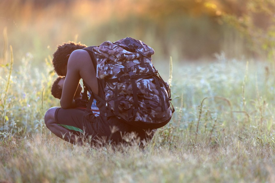 A father kneels down and hold his child in a grassy field.