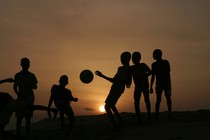 The silhouettes of a group of children kicking a soccer ball in front of the setting sun