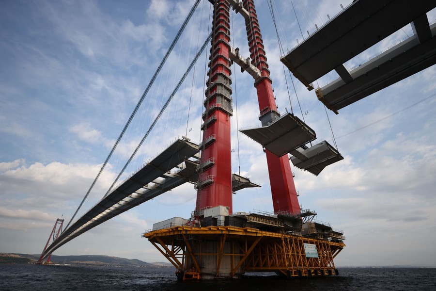 Construction takes place on a very long suspension bridge.