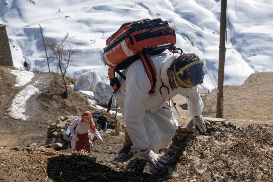 Two health-care workers climb a steep slope, carrying supplies.
