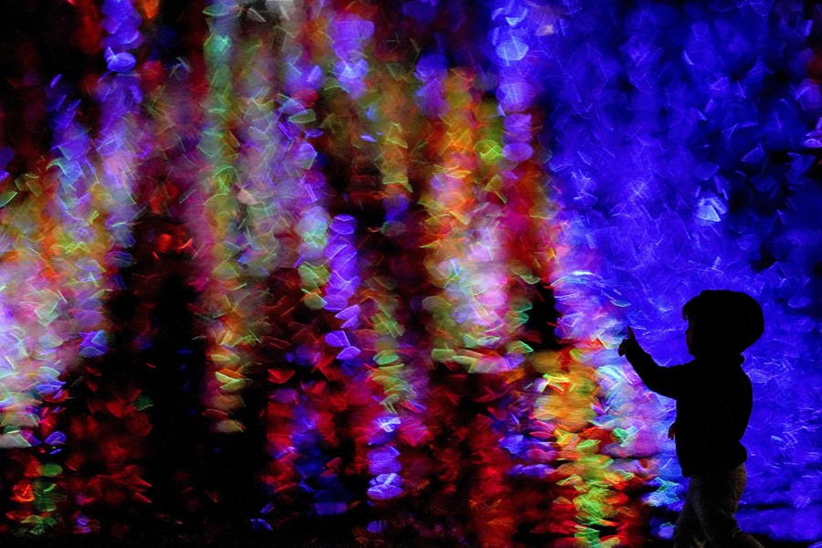 A boy is silhouetted against Christmas lights reflected in a pond.