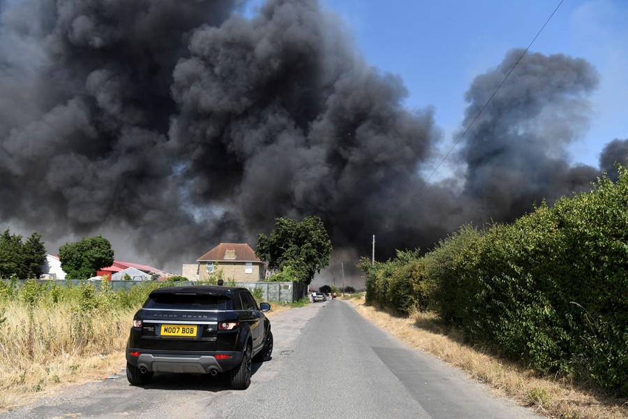 Black smoke rises above houses, seen from a road.