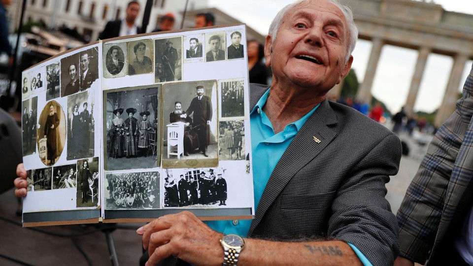 Holocaust survivor Morris Dan shows family photographs as he poses in front of the Brandenburg Gate in Berlin in 2017.