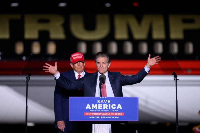 Donald Trump stands behind Mehmet Oz as Oz speaks at a podium