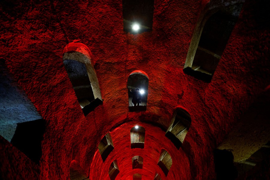 A person stands in an archway inside a deep well, which is bathed in red light.