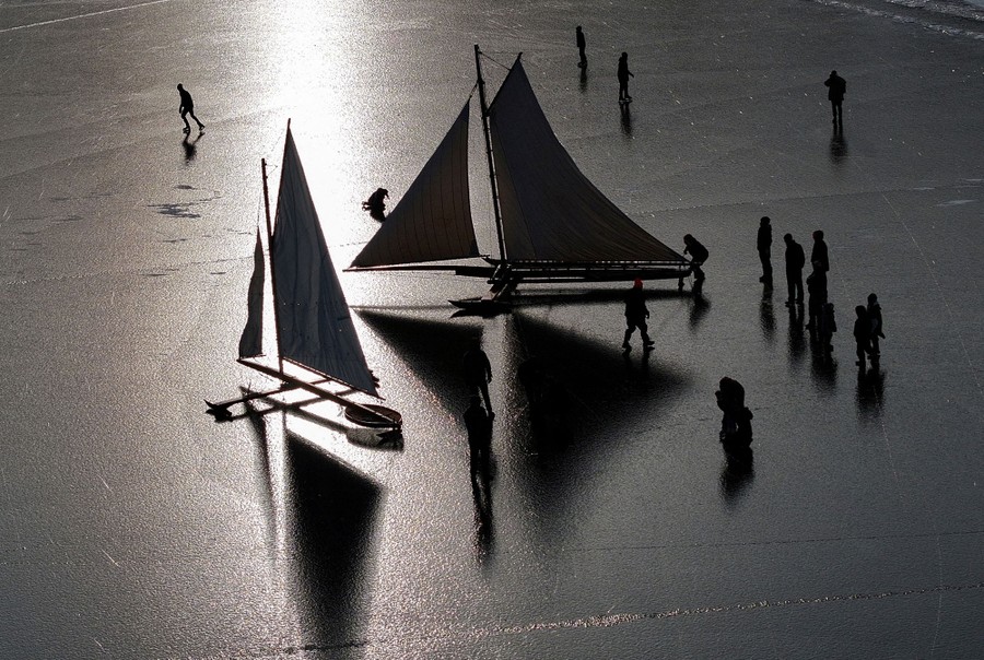 An aerial view of small, slender ice-sailing yachts on a frozen river
