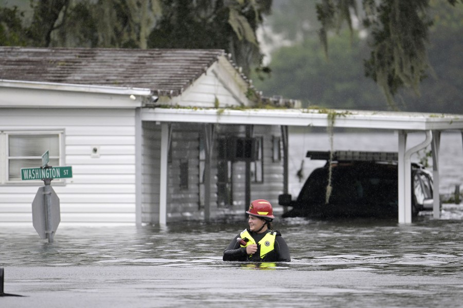 A first responder wades through chest-deep floodwater outside a house.