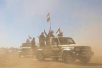 Houthi fighters and tribesmen rally with flags in the back of a pickup truck surrounded by desert dust.