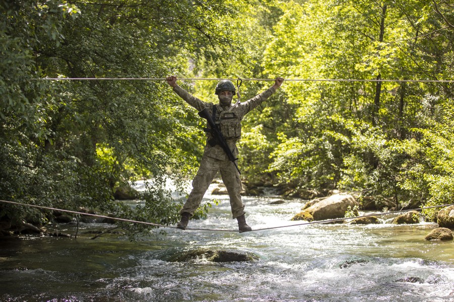 A soldier crosses above a river standing on a rope, holding another rope support above their head.