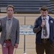 Walton Goggins, as Lee Russell, and Danny McBride, as Neal Gamby, stand in the center of a gymnasium holding microphones. 