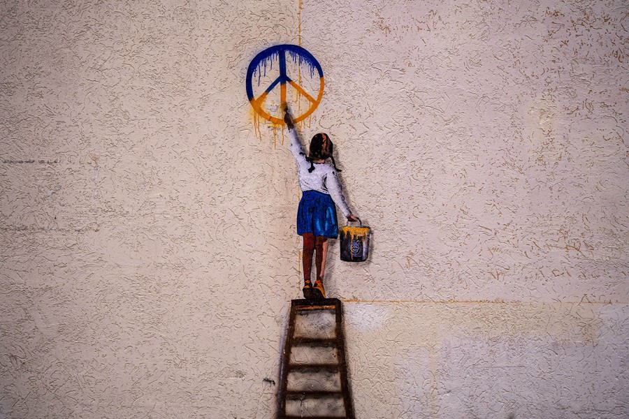 A mural depicts a girl on a ladder painting a peace symbol in blue and yellow, the colors of Ukraine's flag.