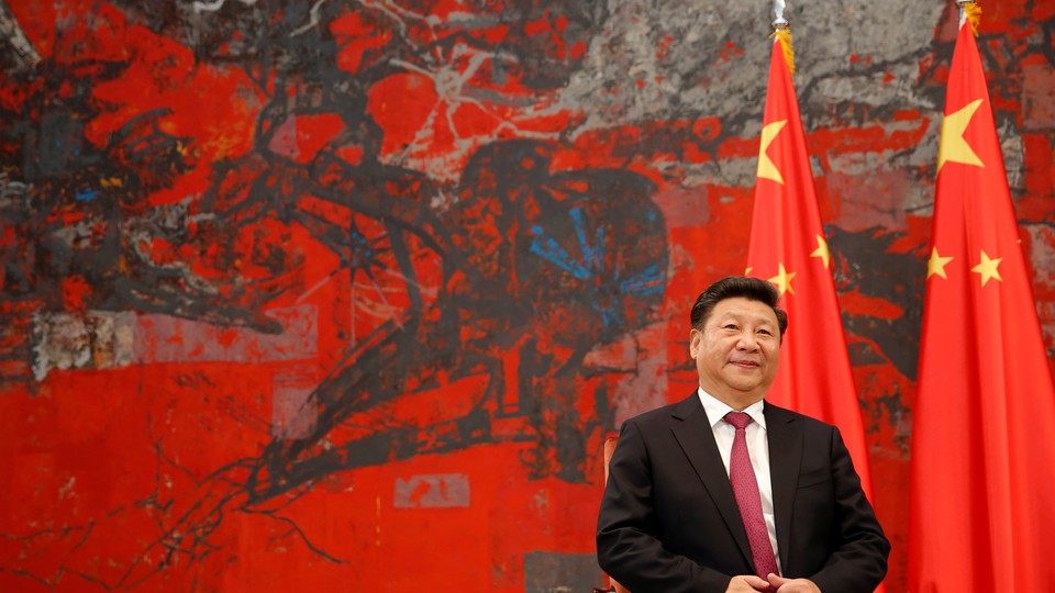 Chinese President Xi Jinping  sits in a chair in front of two Chinese flags.